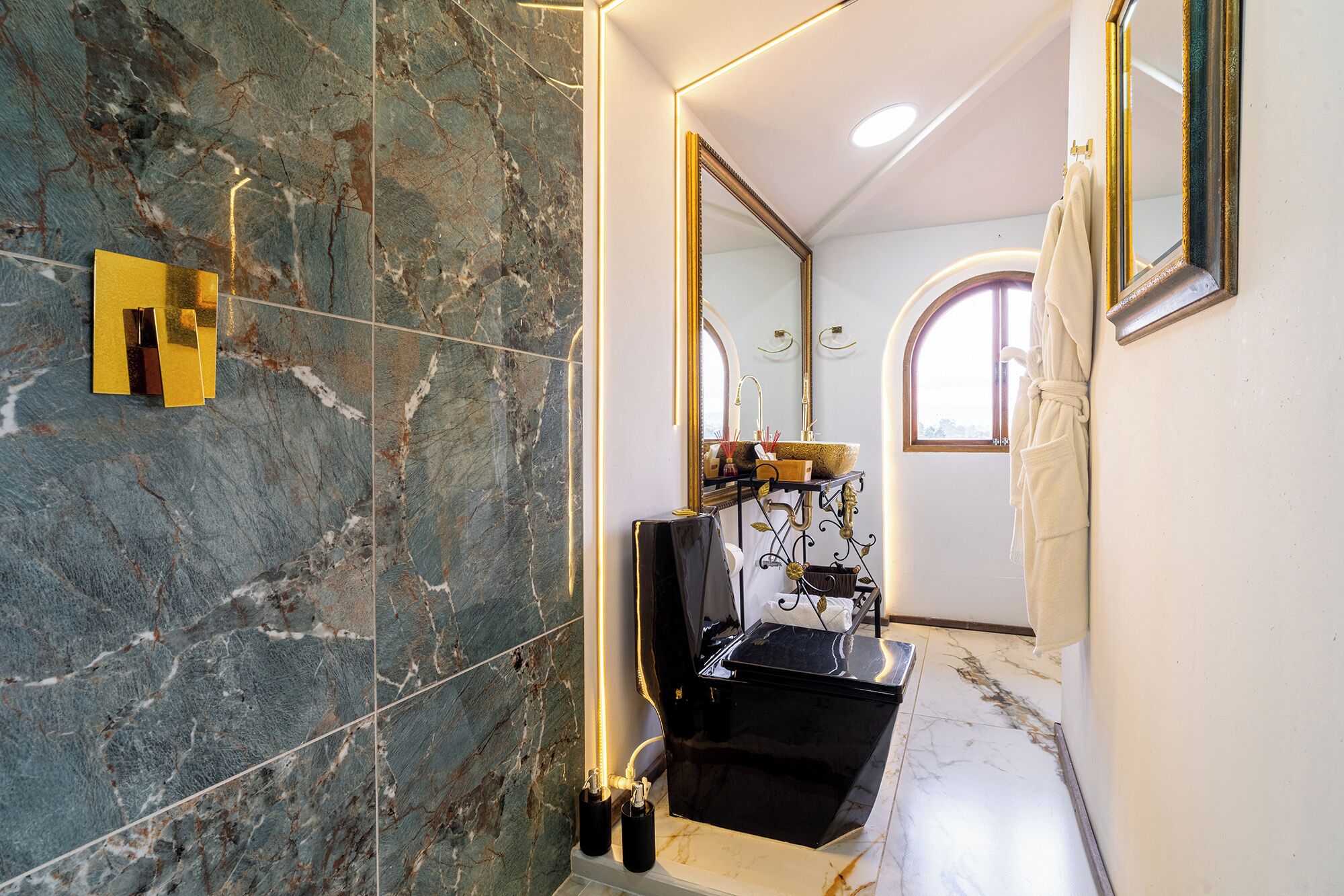 A bathroom with a marble floor, a black sink, and a gold-framed mirror.