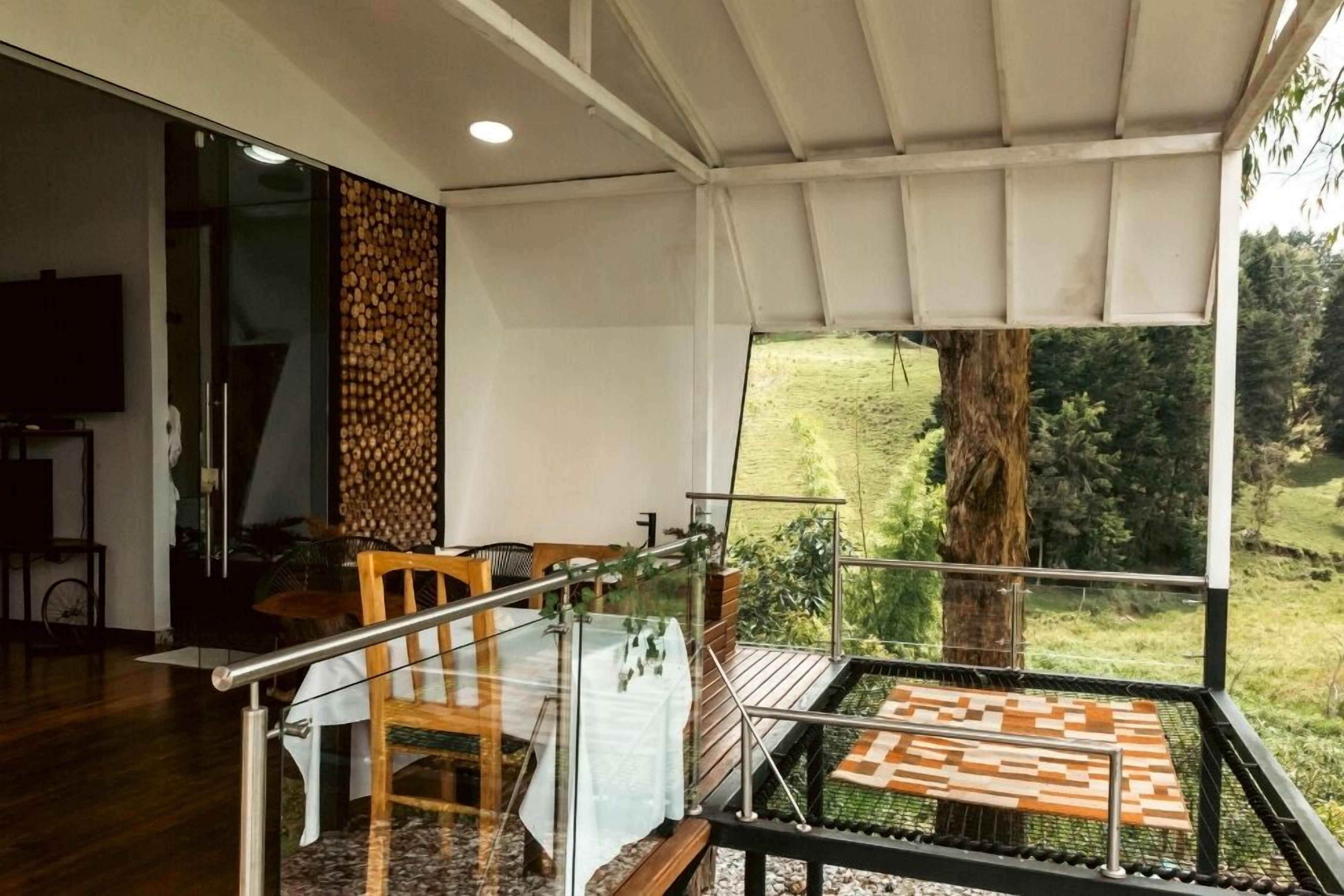 A modern interior with a glass railing, a wooden table, and a view of a lush landscape.