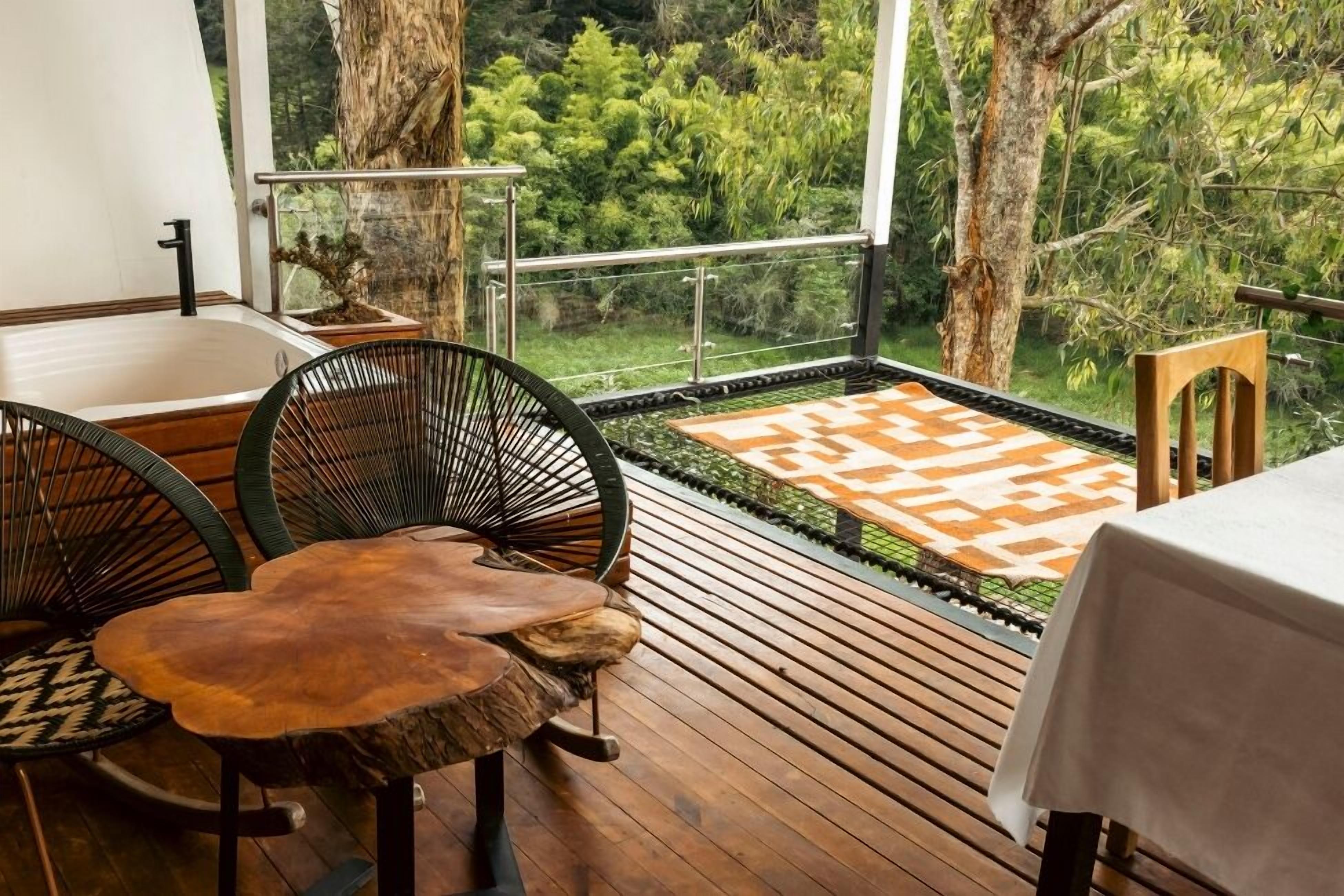 Um deck de madeira com mesa e cadeiras, um pequeno espelho d'água e vista para o verde.