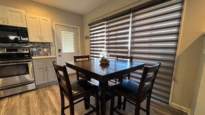 A modern kitchen with built-in appliances, a dining table with chairs, and a large window with blinds.