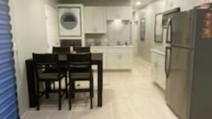 A modern kitchen with white cabinets, a dining area with a table and chairs, and a refrigerator.
