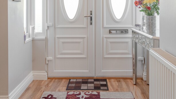 Un pasillo con puertas dobles, un tapete estampado, un jarrón con flores y un radiador.