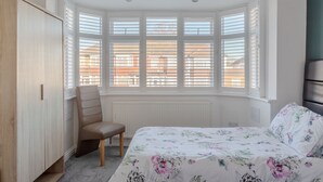 Un dormitorio con ventanal, cama con ropa de cama floral, una silla y un armario.