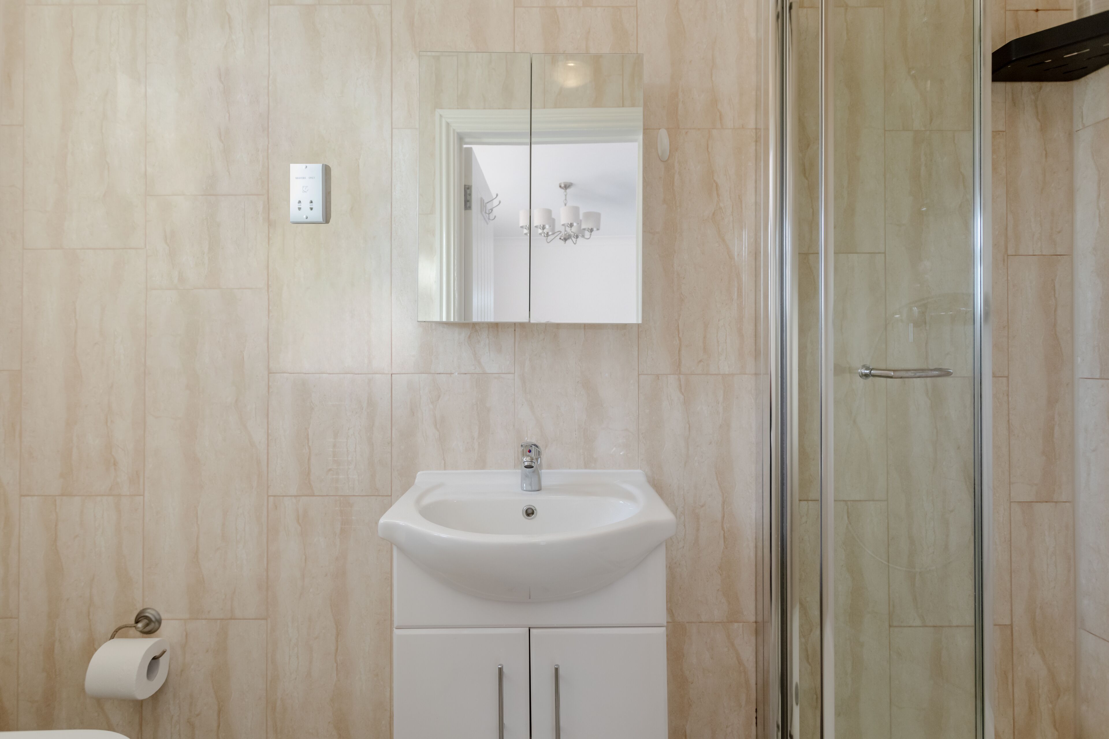 Een badkamer met een wit wastafelmeubel, een spiegel en een douchecabine van glas.