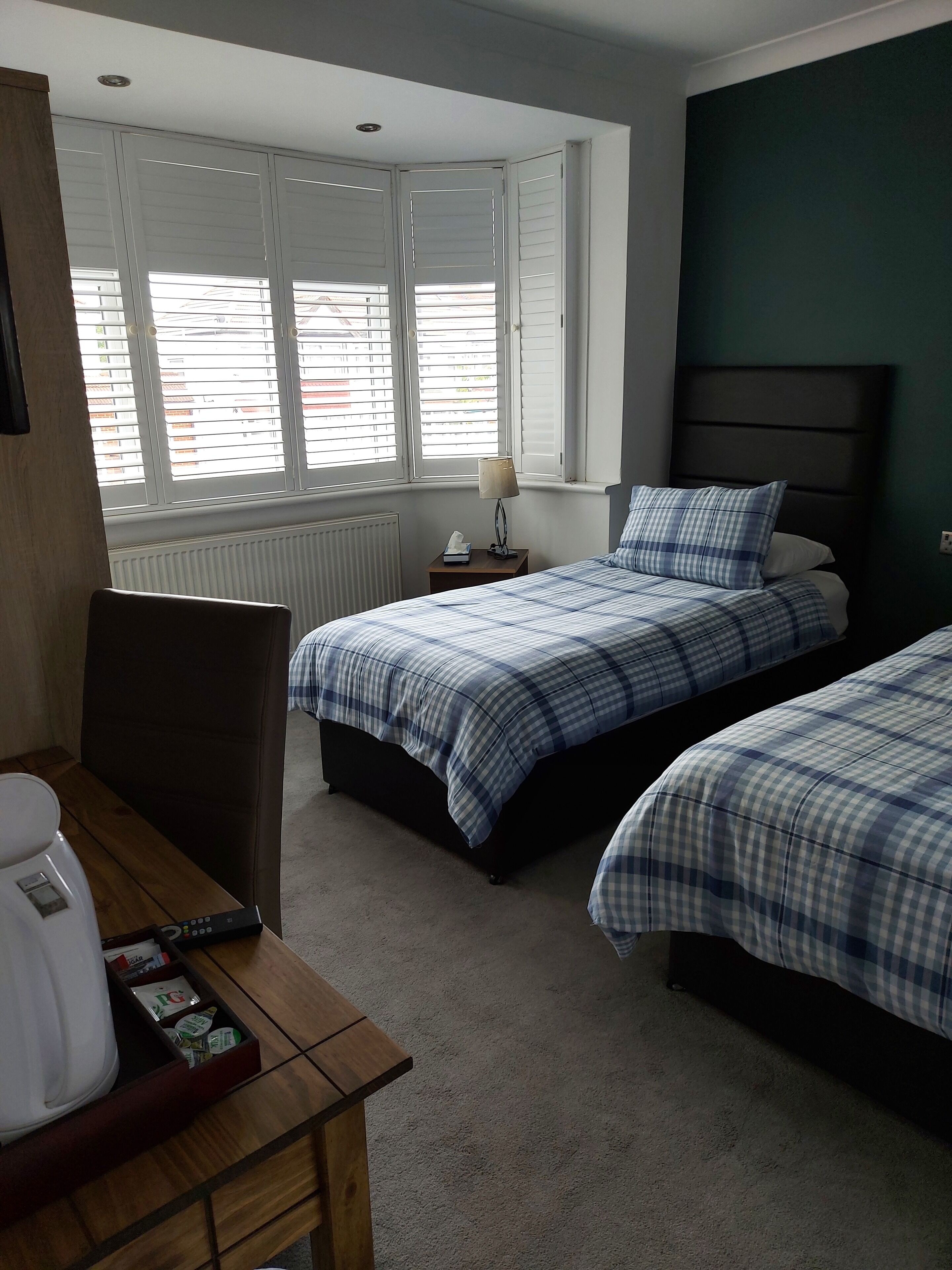 A hotel room with two beds, a desk with a coffee maker, a lamp, and a window with blinds.