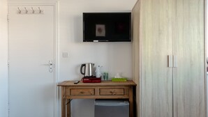 Una habitación pequeña con un escritorio de madera, un televisor montado encima, un armario y una puerta con perchero.