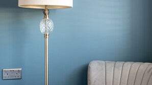 Una habitación con pared azul, un sillón color beige y una lámpara de pie con pantalla de vidrio.