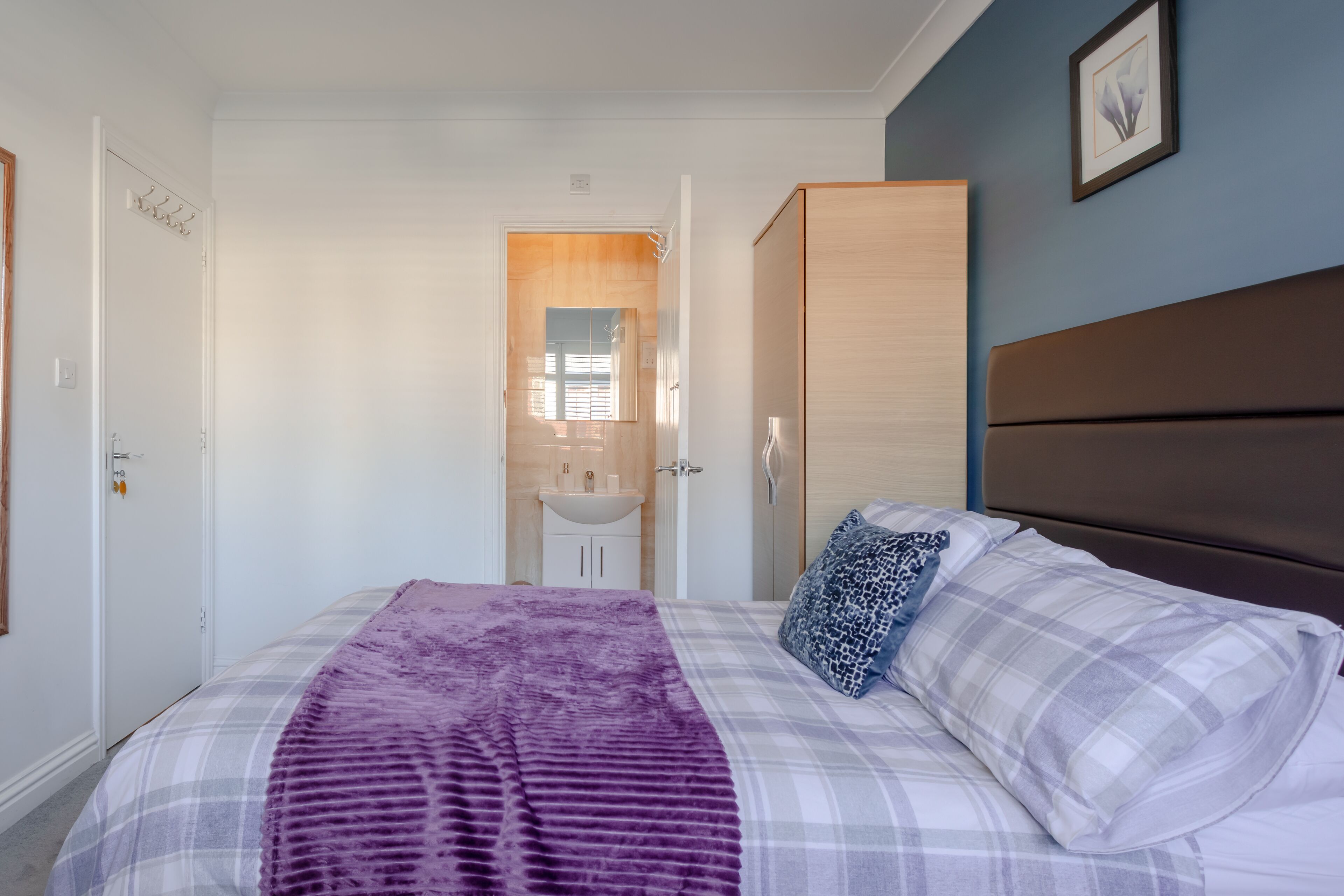 A bedroom with a bed, a wardrobe, a bathroom with a sink, and a door leading to another room.