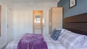 A bedroom with a bed, a wardrobe, a bathroom with a sink, and a door leading to another room.