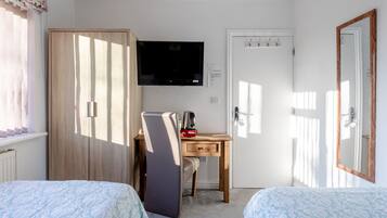 A bedroom with two beds, a desk with a chair, a TV mounted on the wall, and a wardrobe.