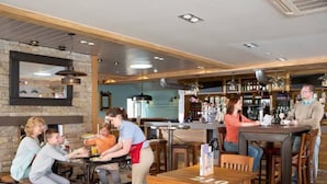 A restaurant with wooden tables and chairs, a bar area, and a stone wall.