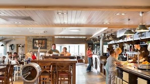 A restaurant with wooden tables and chairs, a bar area, and a kitchen visible in the background.