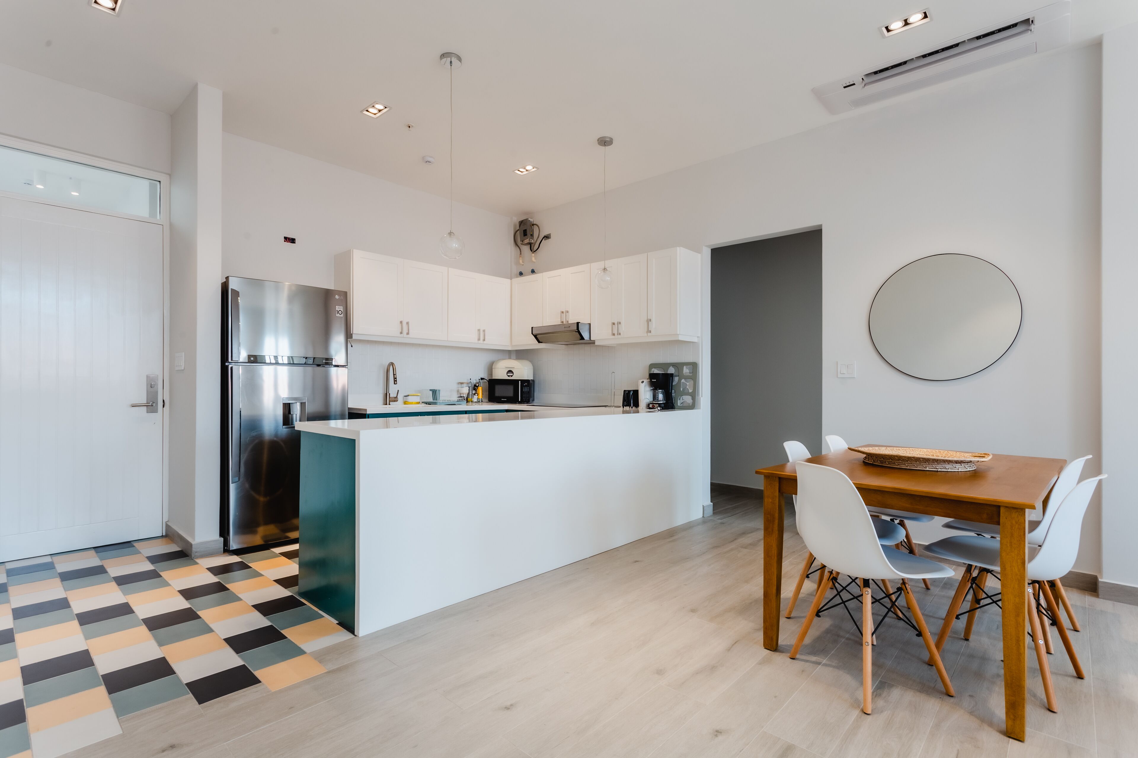 Une cuisine moderne avec des meubles blancs, un îlot central intégré, des appareils électroménagers en acier inoxydable et un coin repas comprenant une table en bois et des chaises blanches.