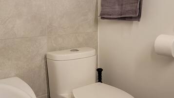 A bathroom with a toilet, a bathtub, a towel rack with towels, and a trash bin.
