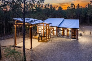 A cabin with a stone exterior, wooden deck, and a covered porch with string lights. - Breakfast at Tiffanys Cabin- Hot Tub/ Swing Bed/ Firepit/ 2-Person Soaker Tub (Broken Bow)