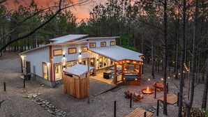 A modern cabin with a large deck, a fire pit, and a covered outdoor seating area.