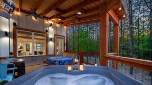 A hot tub with a wooden deck, a dining area with chairs, and a view of a forest.