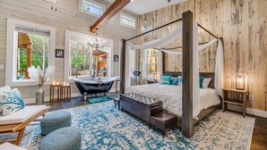 A bedroom with a four-poster bed, a clawfoot bathtub, and a large window with a view of the outdoors.