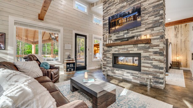 A spacious living room with a stone fireplace, leather sofa, and a large window overlooking a garden.