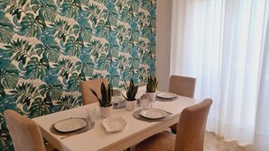 A dining table set with plates, glasses, and cutlery, surrounded by chairs, with a tropical leaf-patterned wallpaper in the background. - Family sized trendy flat in the heart of Marsala with balconies and sea view (Marsala)