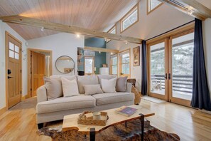 A cozy living room with a sofa, a coffee table, and a large window offering a view of the outdoors. - Quinn Peaks Guest House in the mountains! (Bozeman)