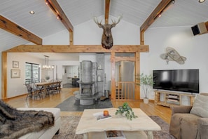Un salón amplio con chimenea de piedra, vigas de madera, un ciervo montado como decoración, un televisor y una zona de estar acogedora.