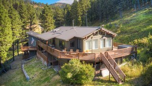 A cabin with a deck, surrounded by forest. - Quinn Peaks Retreat House with a hot tub! (Bozeman)