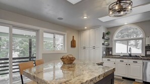 A kitchen with a granite countertop, white cabinets, and a large window. - Quinn Peaks Retreat House with a hot tub! (Bozeman)