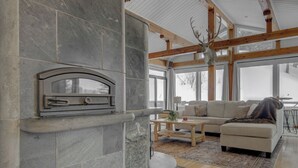 A modern living room with a stone fireplace, a sectional sofa, and a deer head mounted on the ceiling. - Quinn Peaks Retreat House with a hot tub! (Bozeman)