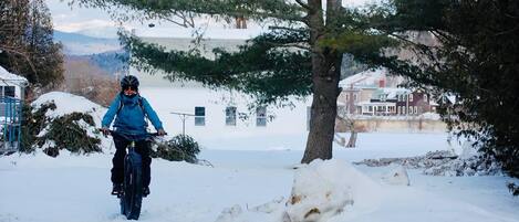 Iemand fietst door een besneeuwd gebied met huizen en bomen op de achtergrond.