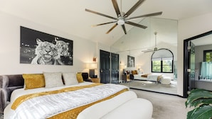 A modern bedroom with a large bed, a ceiling fan, and a painting of tigers on the wall. - Peaceful Luxury Unique 3 BDR Home w/ Cinema & More (Traverse City)