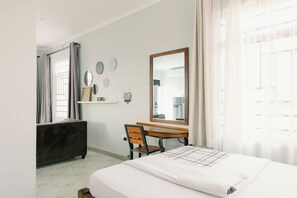 A hotel room with a bed, a desk, a chair, a vanity with a mirror, and a window with curtains. - Sarita Village - Serene Homestay Experience in Arusha's Outskirts. (Arusha)