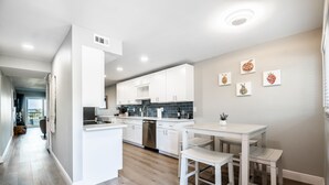 Een moderne keuken met witte kasten, een centraal eiland en een eethoek met witte stoelen.