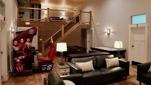 A spacious living room with a high ceiling, a staircase leading to an upper level, a racing game setup, and a fireplace. - Tall Oaks Resort (Willoughby)