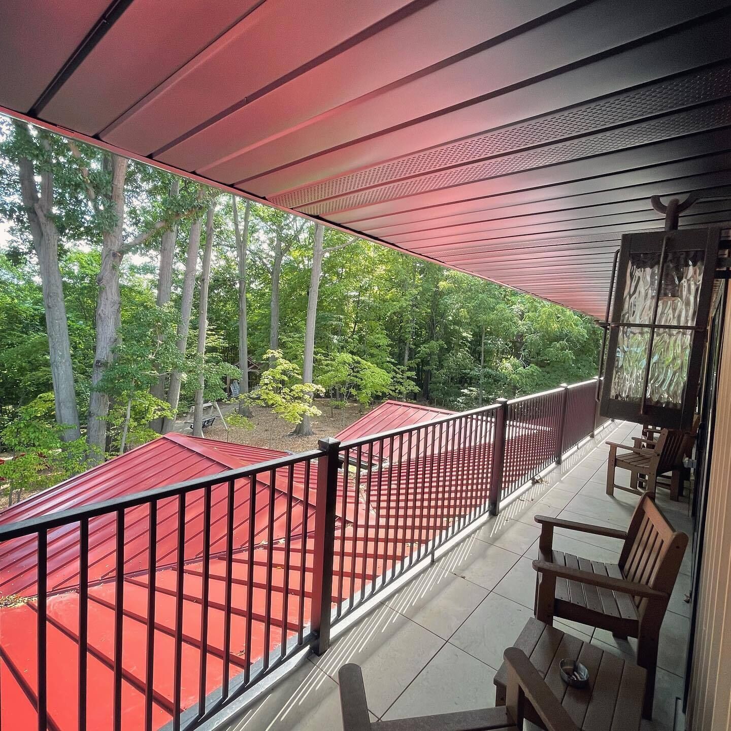 A covered outdoor area with a red floor, wooden benches, and a view of trees.