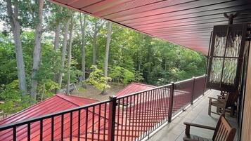 A covered outdoor area with a red floor, wooden benches, and a view of trees.
