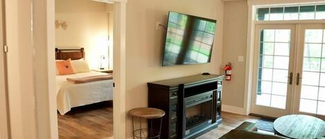 A living room with a fireplace, a television mounted above it, and a bed in the adjacent room.