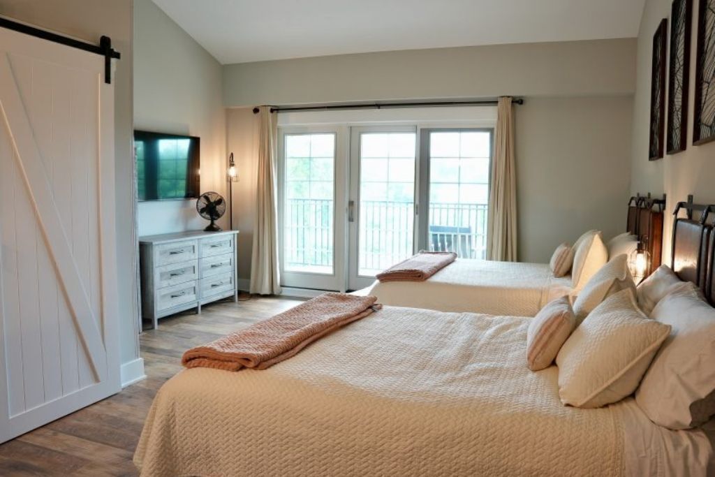 A bedroom with two beds, a dresser, a fan, and a balcony.