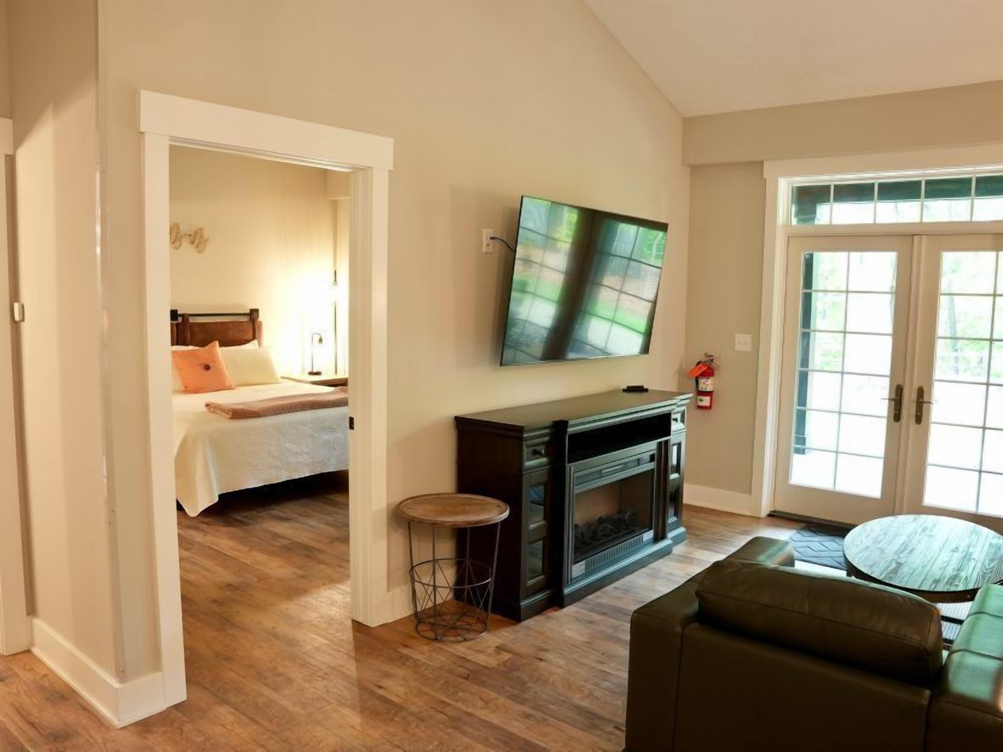 A living room with a fireplace, a television mounted on the wall, and a bed in the adjacent room.