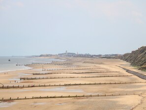A coastal beach with a wooden fence, a lighthouse, and a distant town. - 12 The Dell (Norwich)