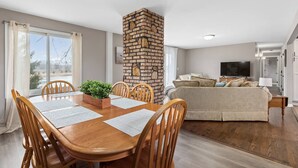 Una sala de estar moderna con chimenea de ladrillo, comedor con mesa y sillas de madera, y un televisor plano grande.