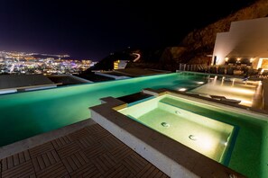 A rooftop infinity pool with a view of a cityscape at night.