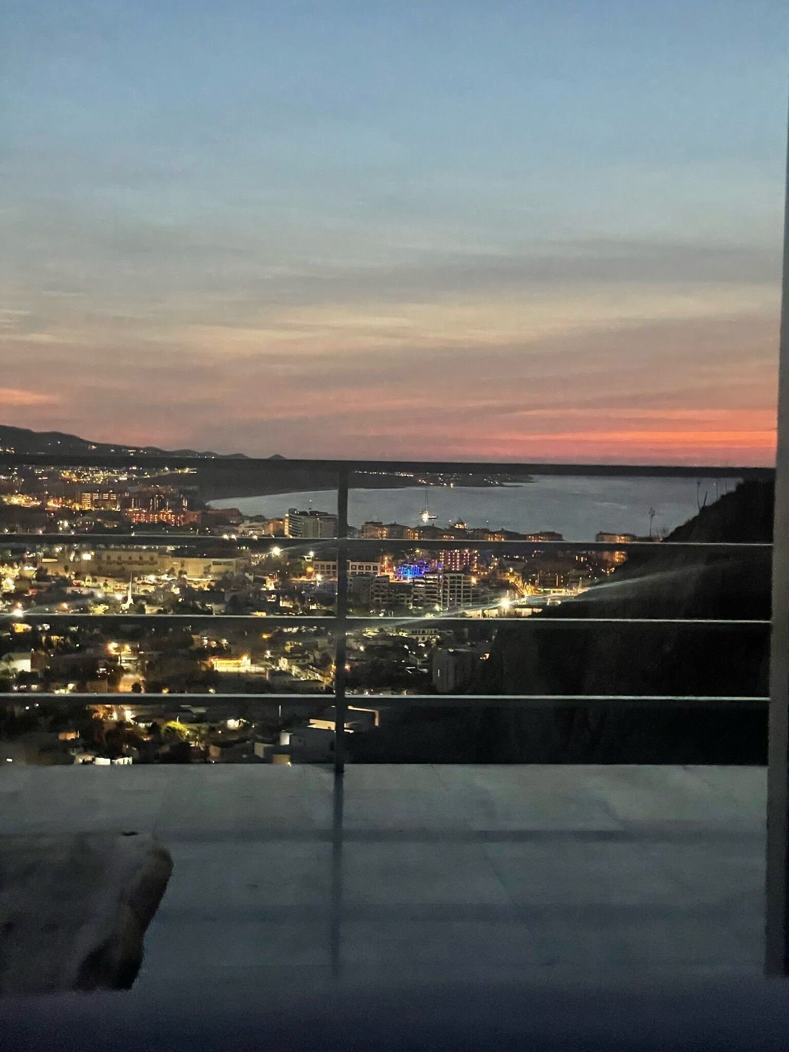 A panoramic view of a city at dusk with a body of water in the foreground and a distant shoreline.