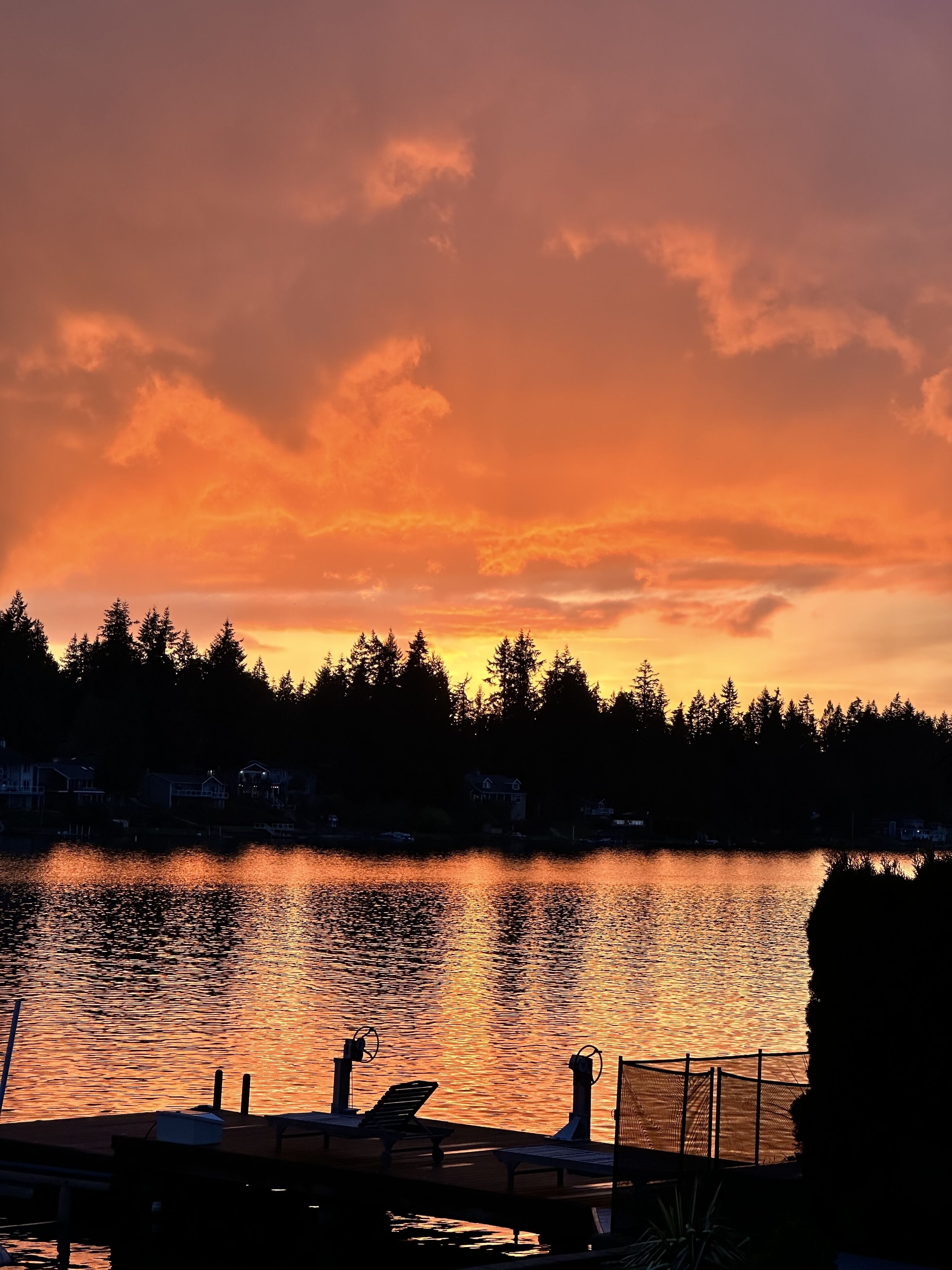 Ein Sonnenuntergang über einem See mit einem Steg und Stühlen.