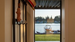 A room with a large window overlooking a lake, a bench, and a wall-mounted coat rack with a hat.