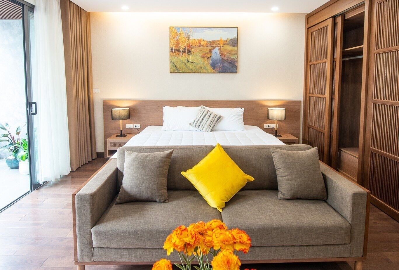 A hotel room with a large bed, two bedside tables with lamps, a wooden wardrobe, and a sofa with cushions.