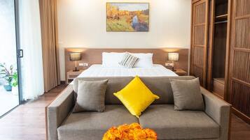 A hotel room with a large bed, two bedside tables with lamps, a wooden wardrobe, and a sofa with cushions.