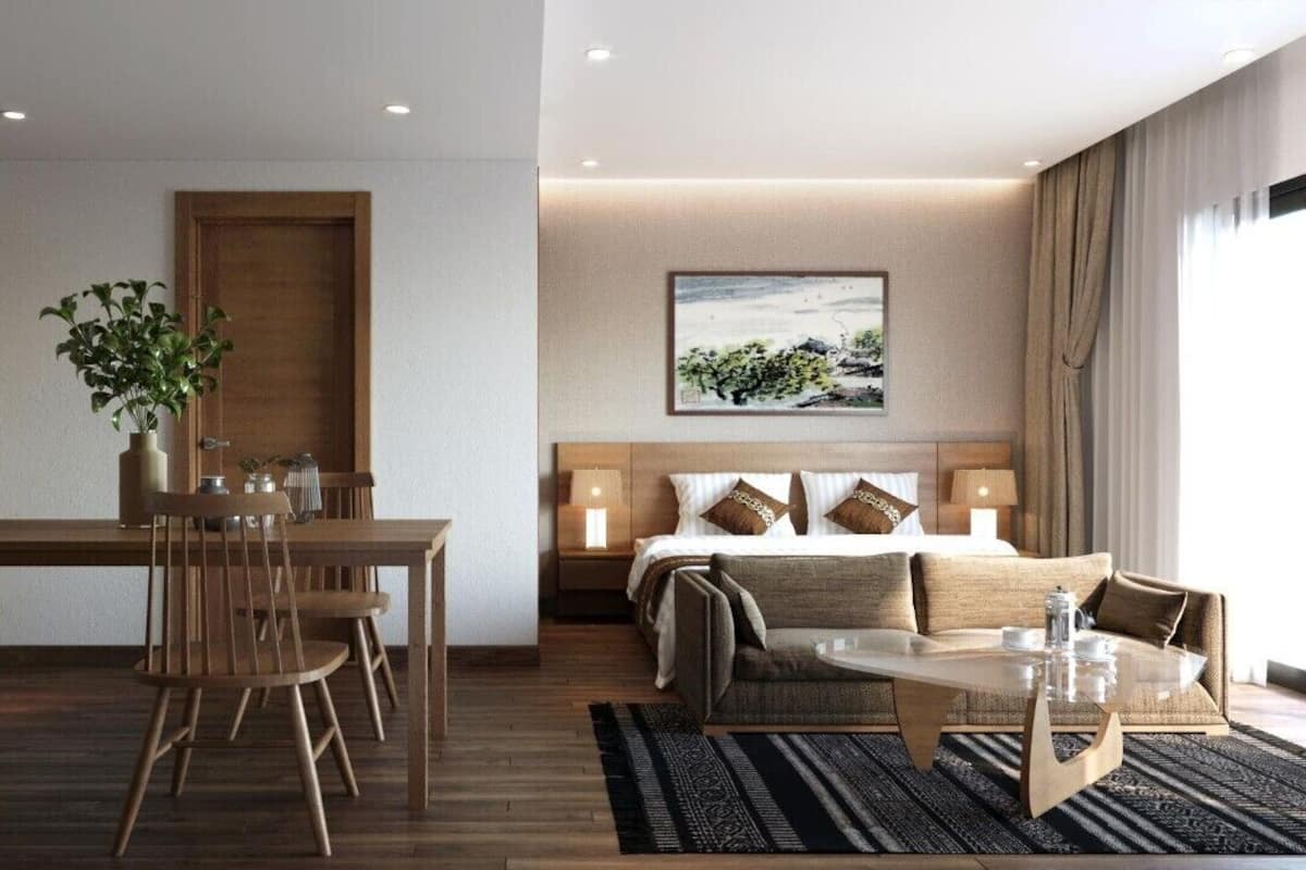 A modern hotel room with a wooden dining table, a sofa, a bed, and a painting on the wall.