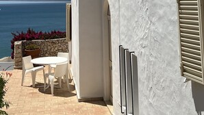 Een wit gebouw met pannendak en schoorsteen, met uitzicht op zee. Er is een terras met een tafel en stoelen.