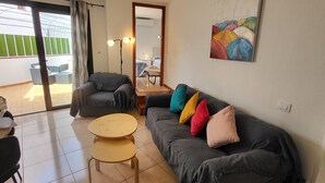 Ein Wohnzimmer mit einer grauen Couch, einem kleinen runden Tisch, einem Deckenventilator und einem farbenfrohen abstrakten Gemälde an der Wand.